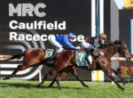 Two jockeys on dark brown horses sprint toward the finish at Caulfield Racecourse, race banners in the background.