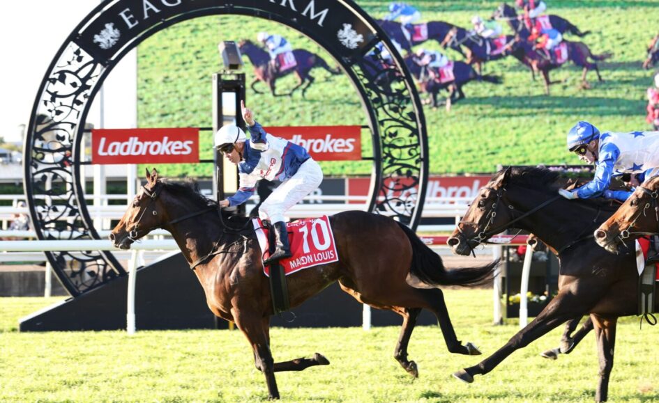 Race finish at Eagle Farm with jockeys on brown horses crossing the line under a decorative arch.