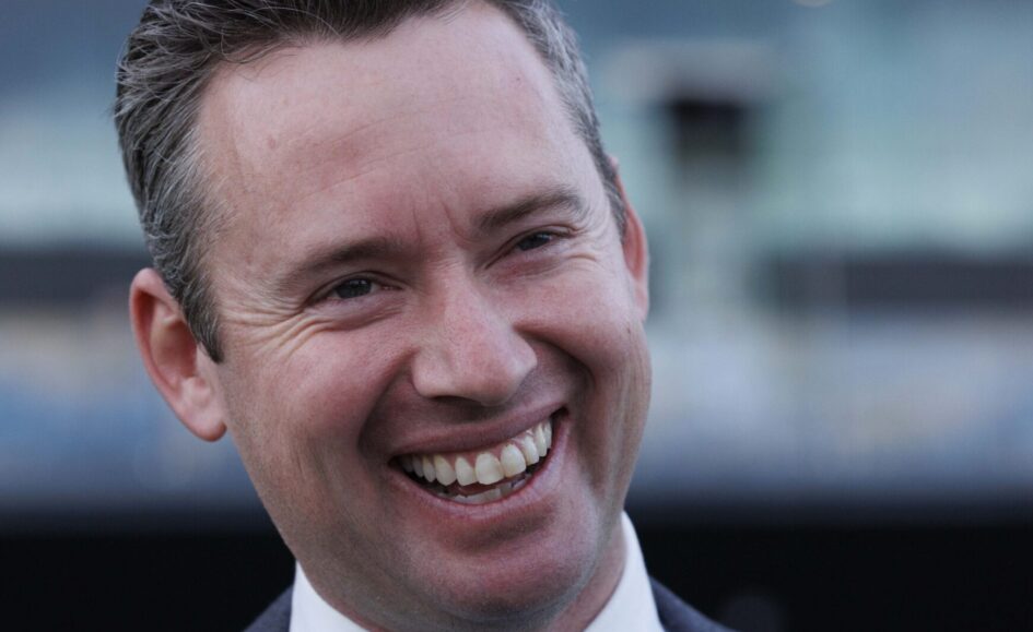 Close-up of a smiling man in a suit, looking off to the side.