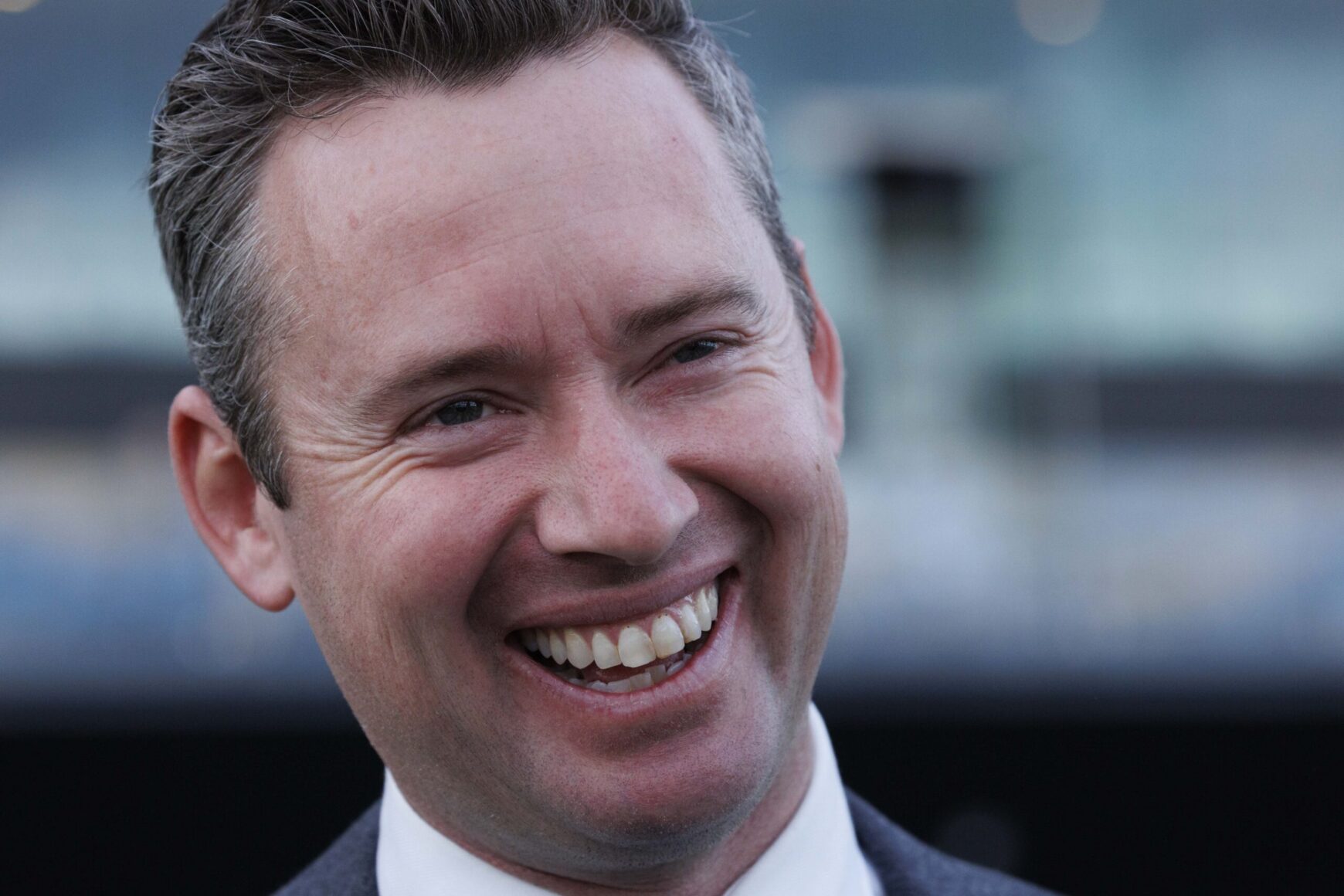 Close-up of a smiling man in a suit, looking off to the side.