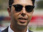 Close-up of a man in a suit wearing black Ray-Ban sunglasses, outdoors.