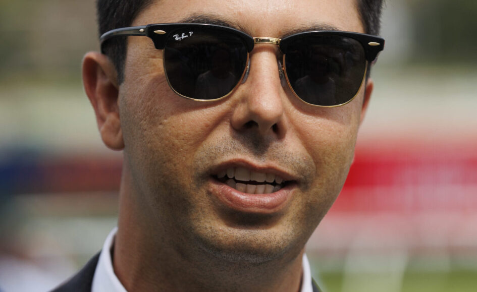 Close-up of a man in a suit wearing black Ray-Ban sunglasses, outdoors.