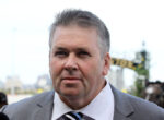 Man in a gray suit and striped tie at an outdoor event, facing the camera with a slight smile.