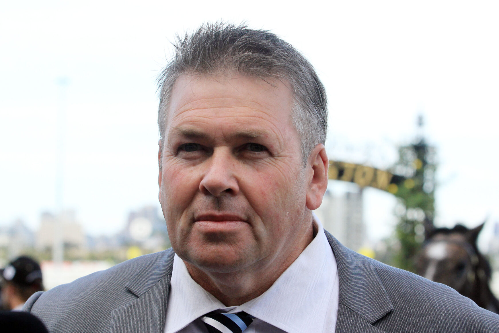 Man in a gray suit and striped tie at an outdoor event, facing the camera with a slight smile.