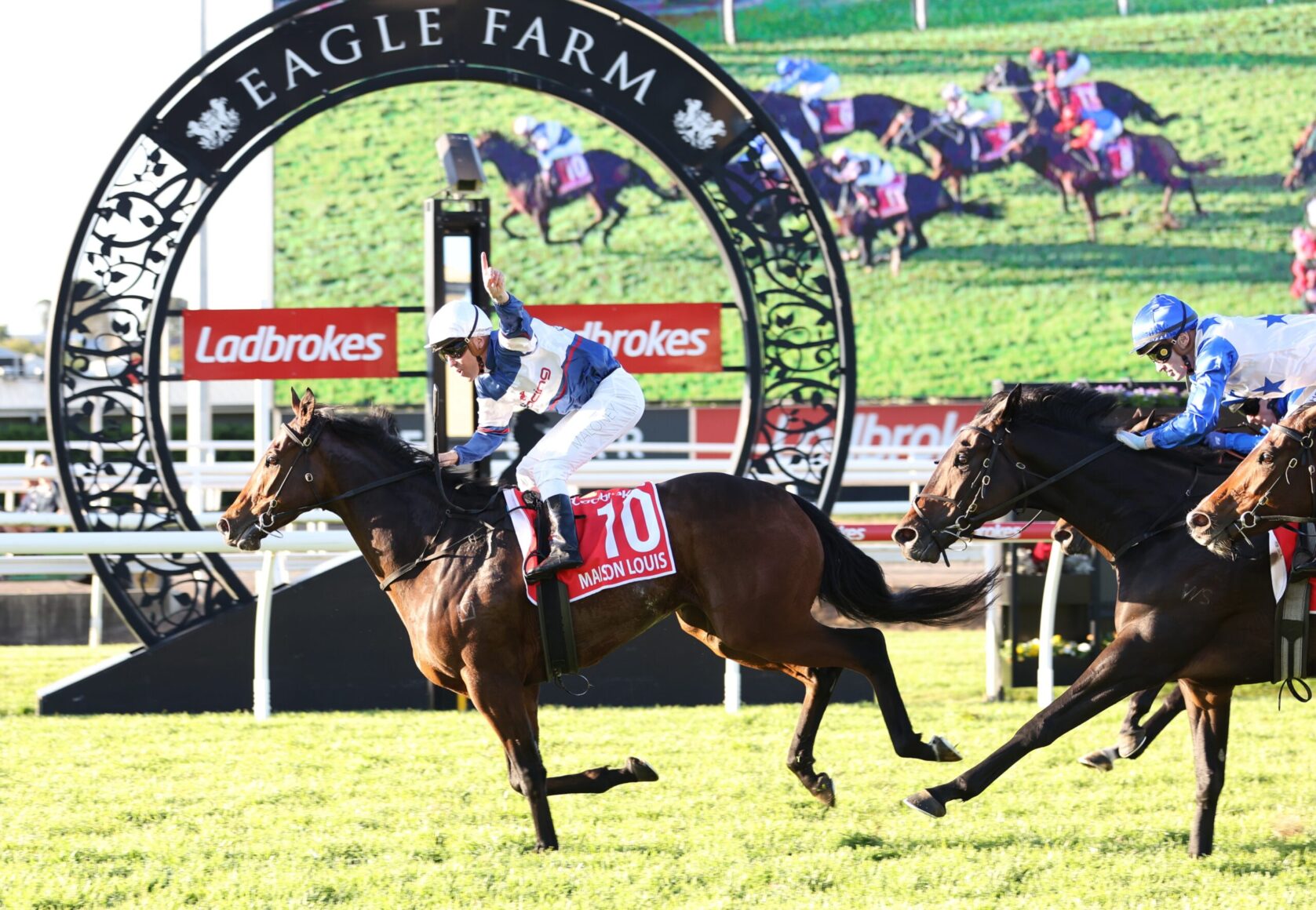 Jockey on horse #10 leads a race at Eagle Farm under a decorative arch with spectators in the background.