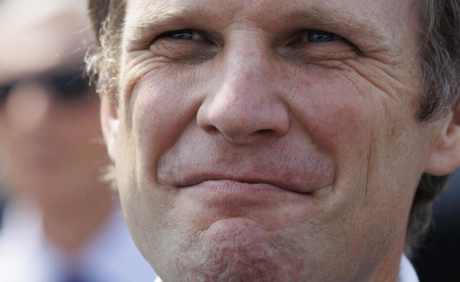 Close-up of a middle-aged man making a puckered lips expression, squinting slightly outdoors, with visible wrinkles and stubble.