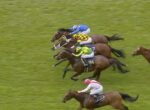Several thoroughbred horses race neck-and-neck on a green turf as jockeys in bright silks lean forward in a crowded finish.