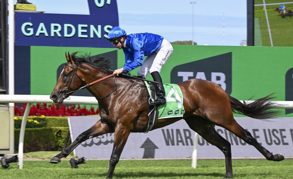 Jockey in blue silks riding a brown galloping horse with green saddle cloth #4 on a racecourse.