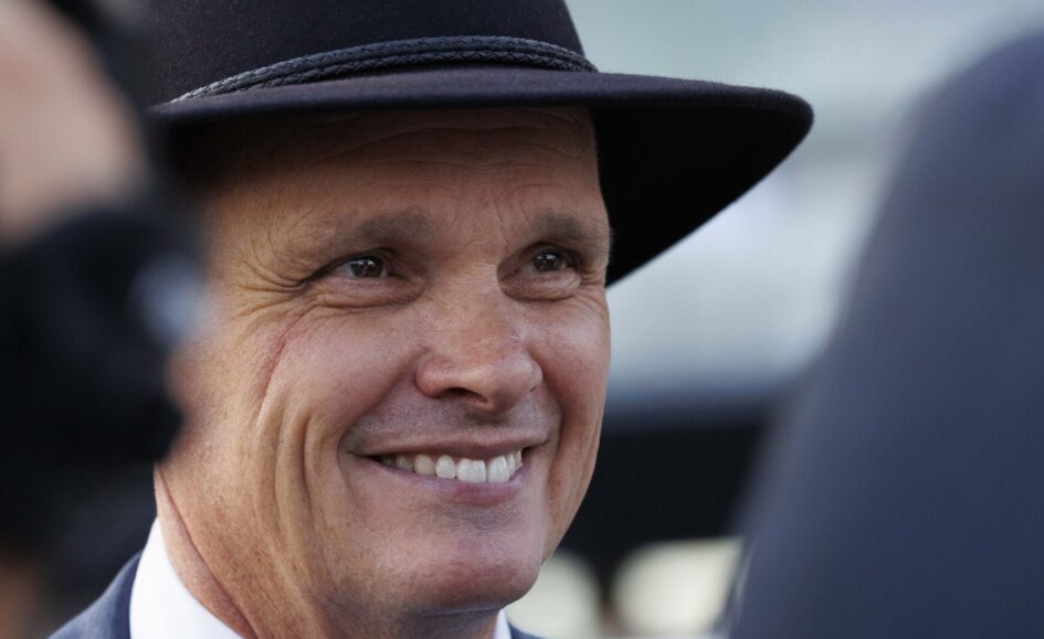 Close-up of a smiling man wearing a black hat and suit, showing warm facial features and a cheerful expression in soft focus backdrop.