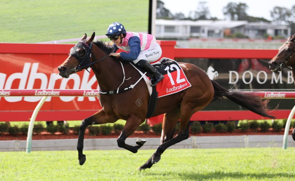 Jockey in pink-and-white silks rides a brown horse over a red fence during a race.