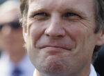 Close-up of a man making a playful, puckered expression with pursed lips and squinting eyes at camera.