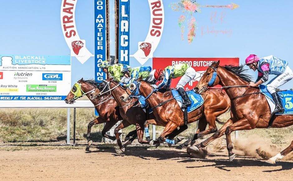Thoroughbreds and jockeys sprint a dirt racetrack under a blue sky, banners visible in the background.