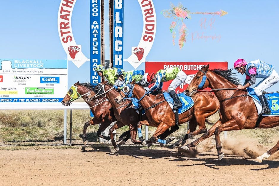 Thoroughbreds and jockeys sprint a dirt racetrack under a blue sky, banners visible in the background.