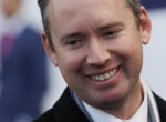 Close-up portrait of a smiling man looking slightly to the side, wearing a scarf and dark coat.