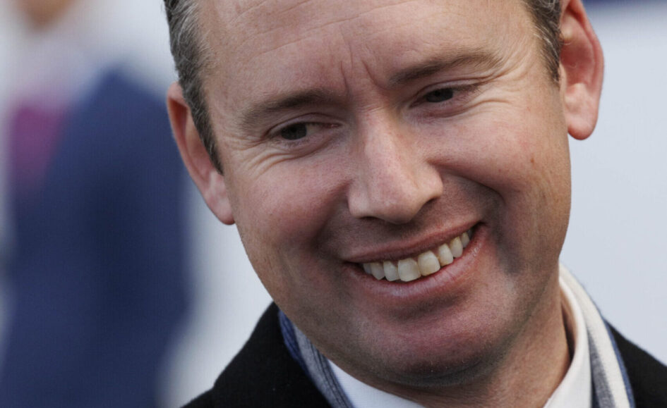 Close-up portrait of a smiling man looking slightly to the side, wearing a scarf and dark coat.