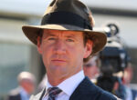 Close-up of a man in a pinstripe suit and brown fedora at an outdoor event.
