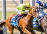 Horse race in progress: a brown horse with blue saddlecloth numbered 35 leads, ridden by a jockey in bright lime-green silks and gold helmet, close to a second rider in a checkered outfit behind.Significant motion and competition conveyed without extra details.