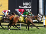 Finish-line action at Caulfield Racecourse with three jockeys in red, white, and green silks racing neck-and-neck toward the line.