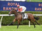 Jockey in red sleeves and pink helmet riding a brown racehorse (number 1) on a grassy race track, with Royal Randwick signage in the background.