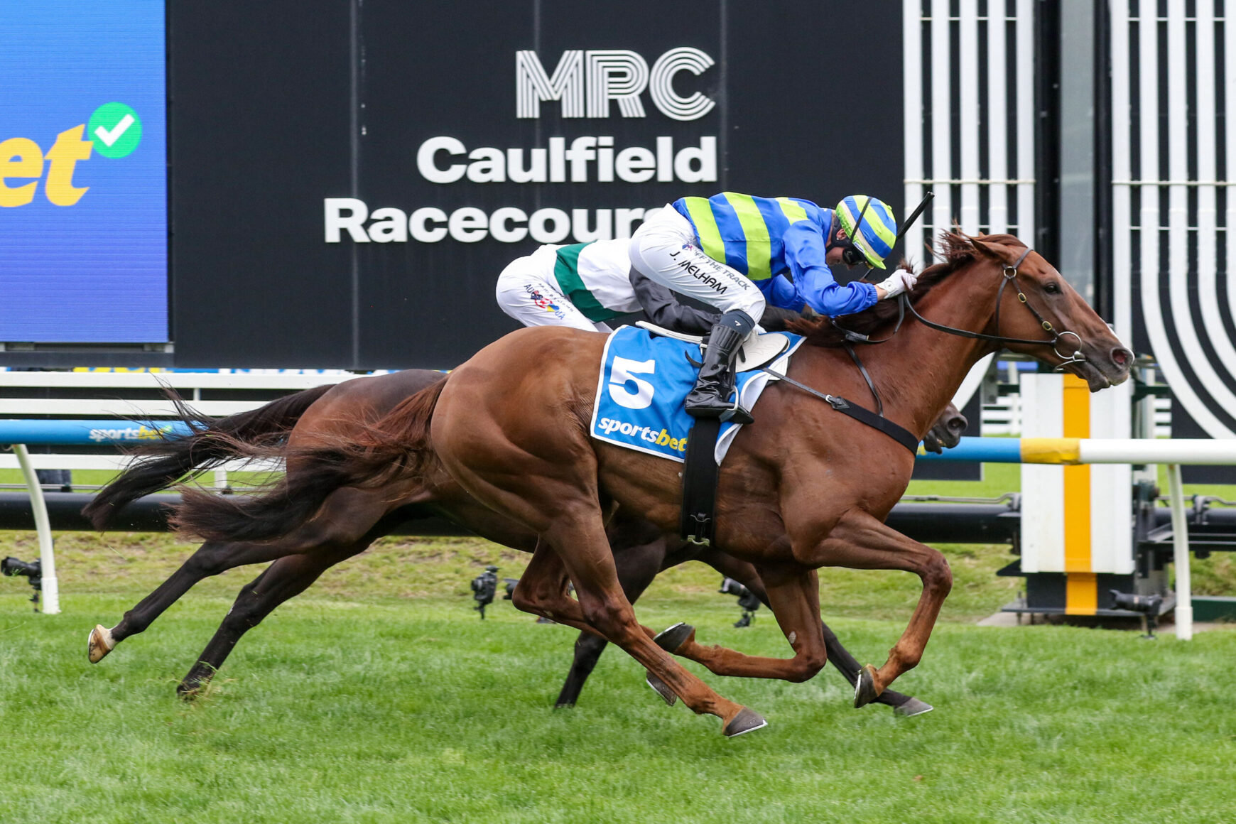 Two jockeys on racing horses sprinting side by side at Caulfield Racecourse.