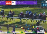 Group of horse racing on a turf track around a bend, jockeys in colorful silks, with race graphics showing Canterbury 1900m and leading Dubai Warrior.