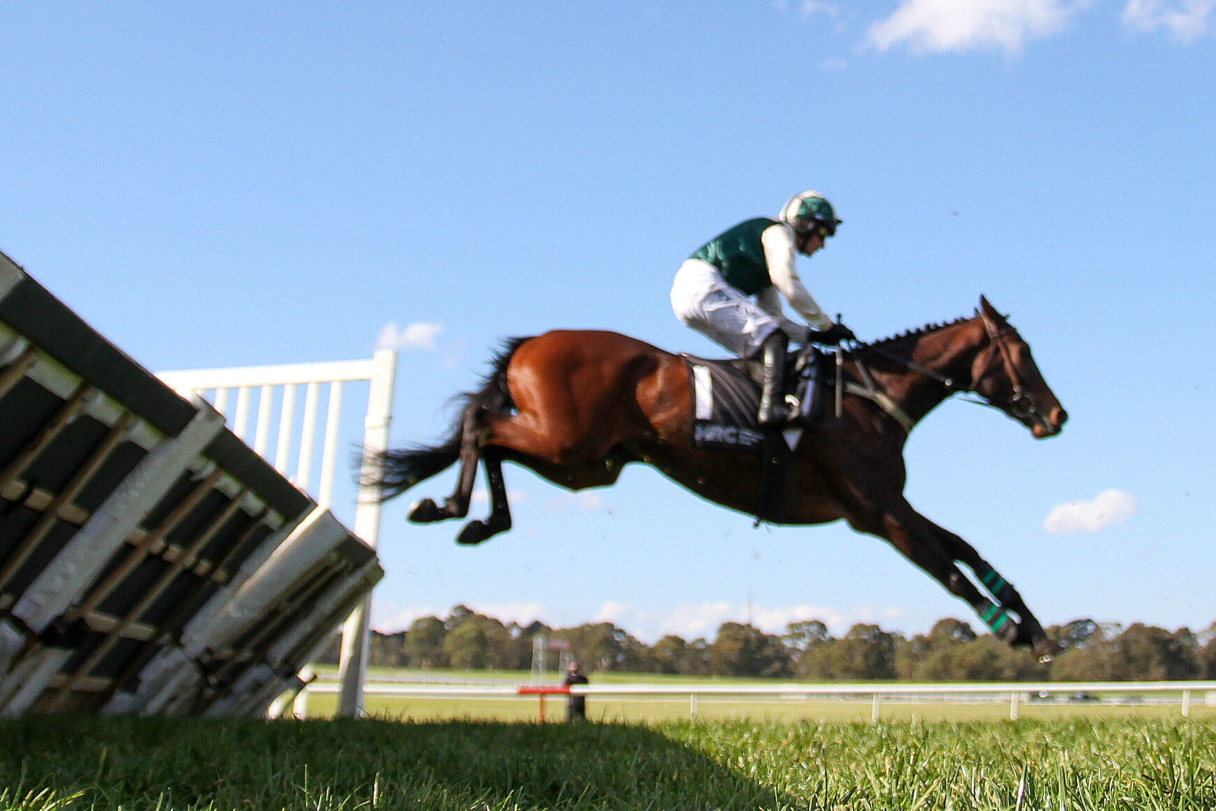Horse and rider in mid-air clearing a wooden jump on a sunny day during show jumping competition