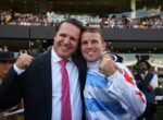 Two men pose and smile with arms around each other at a crowded event.