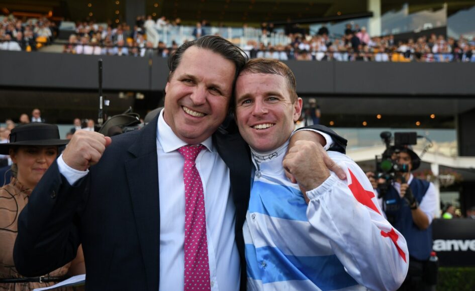 Two men pose and smile with arms around each other at a crowded event.