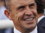 Close-up of a smiling middle-aged man in a suit, showing wrinkles and teeth.