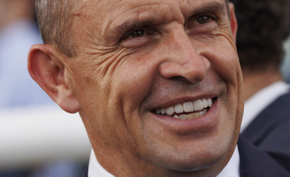 Close-up of a smiling middle-aged man in a suit, showing wrinkles and teeth.