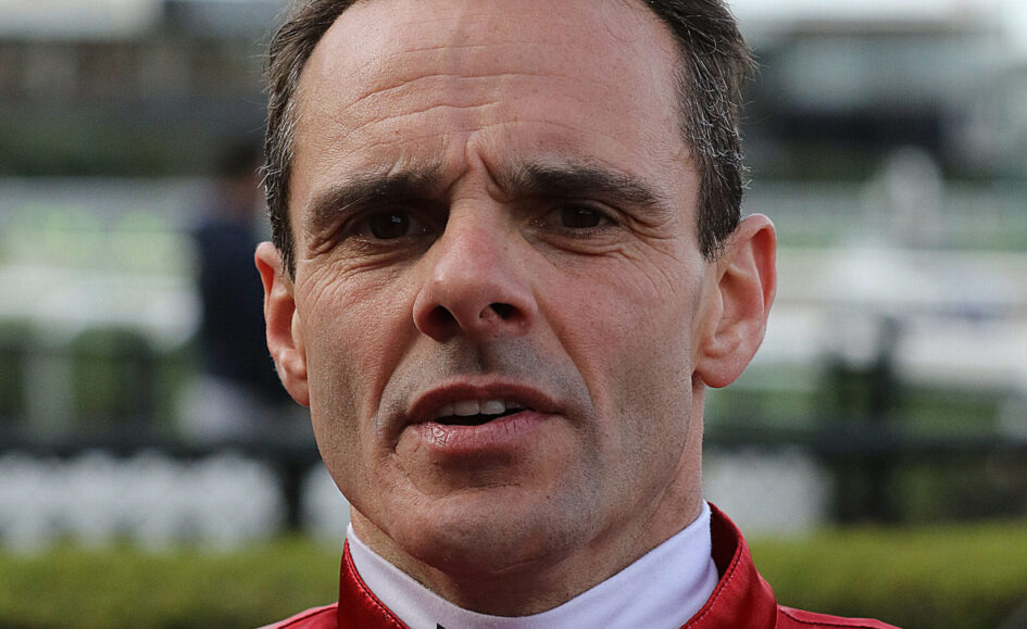 Close-up of a man in a red racing suit outdoors, looking serious with a furrowed brow.