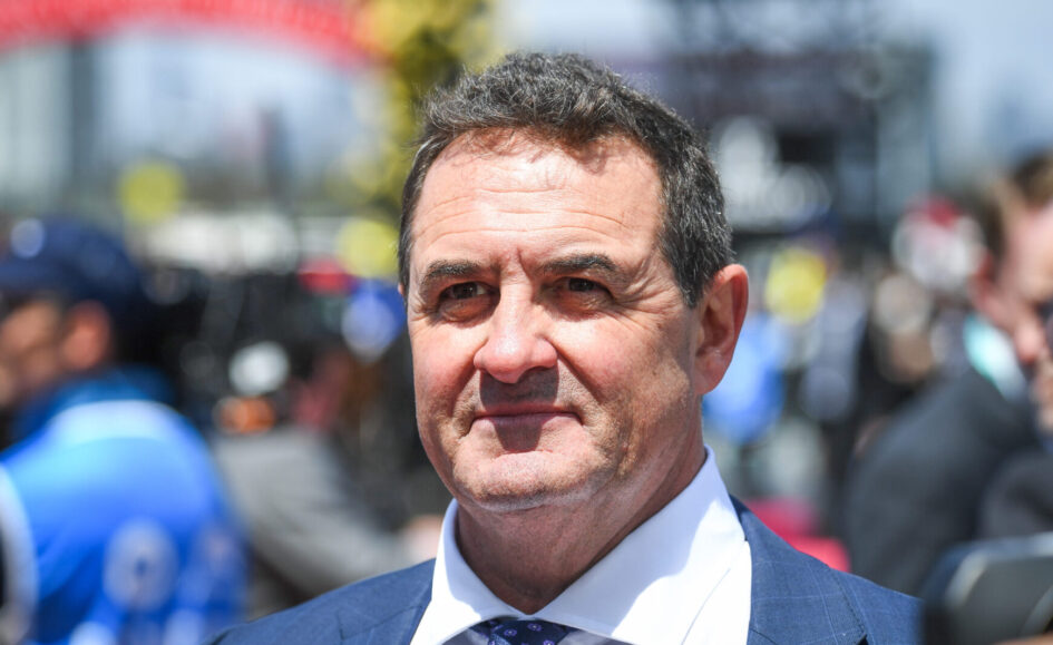 Portrait of a middle-aged man in a blue suit and patterned tie, outdoors at a crowd-filled event, smiling slightly.