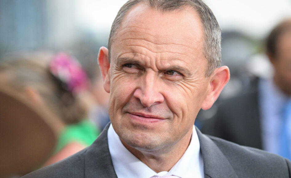Close-up of a middle-aged man in a gray suit and pink tie, outdoors, with a slight smile on his face.