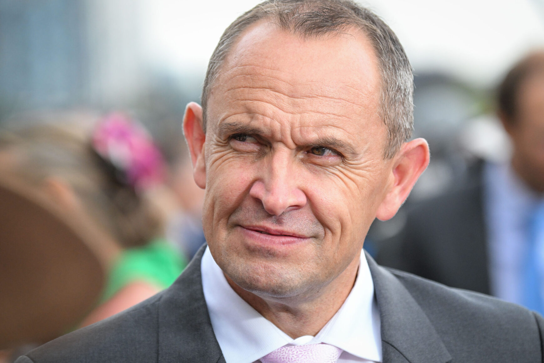 Close-up of a middle-aged man in a gray suit and pink tie, outdoors, with a slight smile on his face.